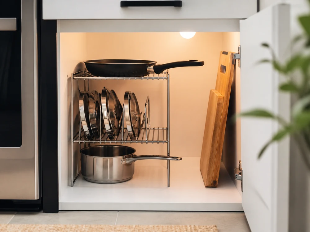 Wire shelf organizer in a lower kitchen cabinet holding pans and lids with clear reach space